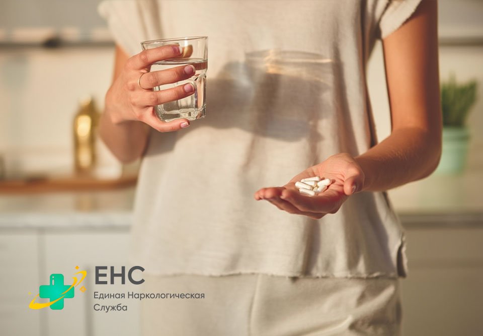 Женщина держит стакан воды и горсть таблеток